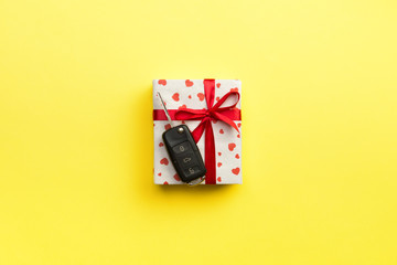 Car key on paper gift box with red ribbon bow and heart on yellow table background. Holidays present top view concept