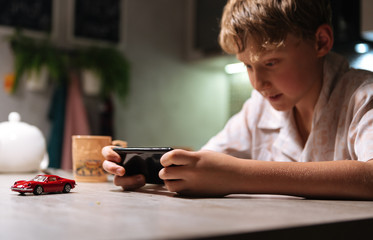 Young boy playing video game using smartphone on the kitchen table.