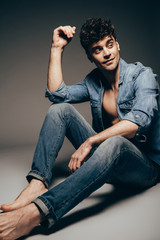 handsome barefoot fashionable man posing in jeans clothes on dark grey