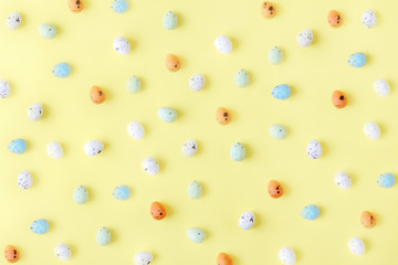 Small colored Easter eggs on a bright yellow background, top view