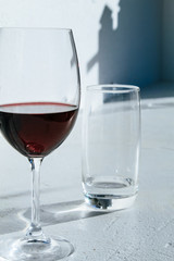 Glass of red wine standing on a white surface in front of an almost empty water glass
