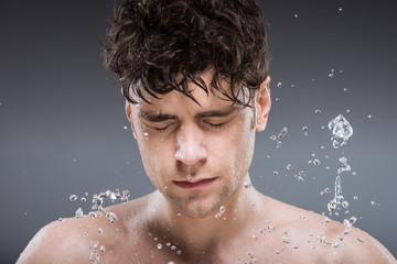 young man washing face with water, isolated on grey