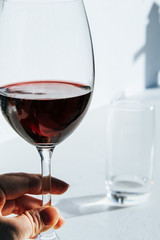 Woman's hand holding a glass of red wine in front of a white wall with bright summer light