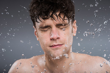 handsome man washing face with water, isolated on grey