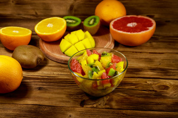 Tasty fruit salad in glass bowl and fresh fruits on the wooden table