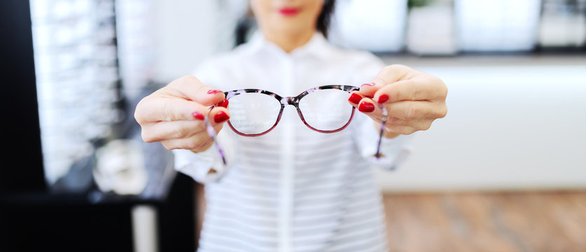 Woman at optician holding eyeglasses she want to buy. Selective focus on glasses.