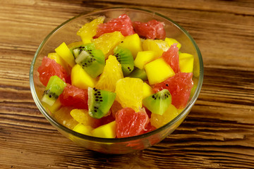 Tasty fruit salad in glass bowl on the wooden table