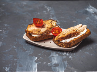 Two turkey sandwiches with ham, curd cheese and cherry tomatoes on a gray wooden background.