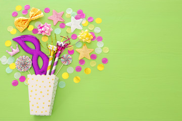 carnival party celebration concept with mask and colorful party accessories over green wooden background. Top view. Flat lay.
