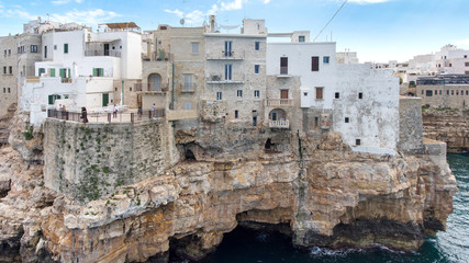 Fototapeta na wymiar Beautiful view of old town in Polignano a Mare in Italy. Houses and buildings built on cliffs next to ocean or sea. Luxury lifestyle at the edge of the world. Concept of travelling and summer holidays