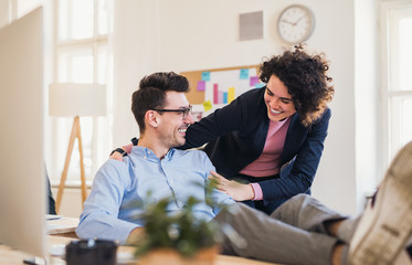 Obraz premium Two young cheerful businesspeople in a modern office, feet on desk.
