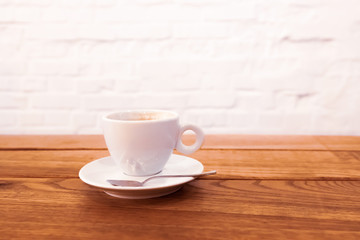 Close up white coffee cup with freshly brewed coffee and a spoon on a saucer stands on a dark wooden table.
