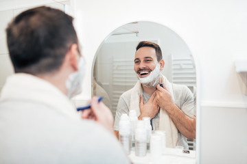 Happy handsome man shawing with razor in the bathroom.