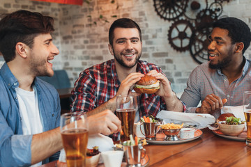 Diverse friends eating burgers and drinking beer in pub