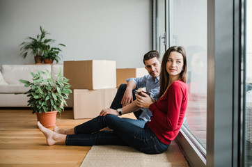 Young couple with cardboard boxes moving in a new home, sitting on a floor.