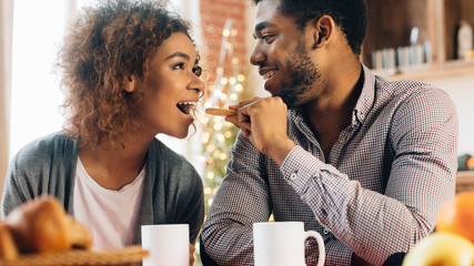 Young black couple feeding each other in kitchen