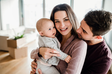 Obraz premium A portrait of young couple with a baby and cardboard boxes moving in a new home.
