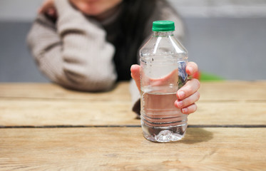 Girl holds in her hand a bottle of water on the table. Clean water for a healthy lifestyle