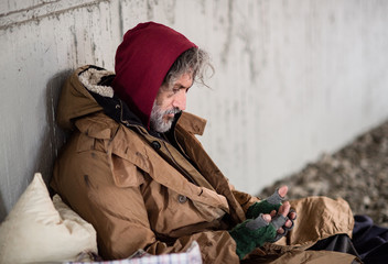 Homeless beggar man sitting outdoors in city asking for money donation.
