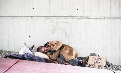 Homeless beggar man lying on the ground outdoors in city, sleeping. Copy space.