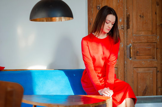 beautiful young slim woman dressed in a bright red dress with a skirt. Poses for a photo in an old-fashioned room with an old decor