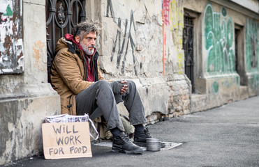 Homeless beggar man sitting outdoors in city asking for money donation. - Powered by Adobe