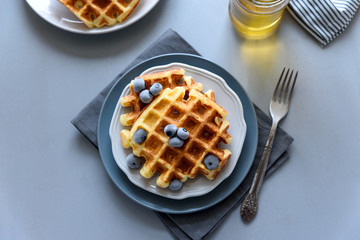 Belgian waffles with blueberries and honey on gray wooden background. Homemade healthy breakfast. Selective focus