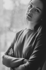 black and white photo of a stylish business woman with a serious facial expression. She is standing by the window with a backlight with her hands folded on her chest