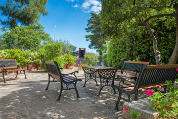 Vintage Italian style garden furniture set up on a terrace next to a villa. Bright red flowers in the front.