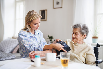 Obraz na płótnie Canvas A health visitor measuring a blood pressure of a senior woman at home.