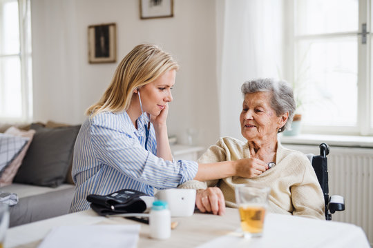 A health visitor examining a senior woman with a stethoscope at home.