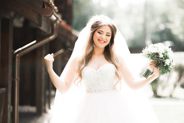 Naklejka premium Beautiful bride in elegant white dress holding bouquet posing in park