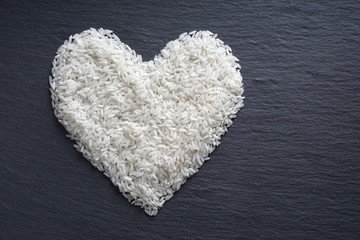 white long-grained rice in heart shape on black slate serving board                               