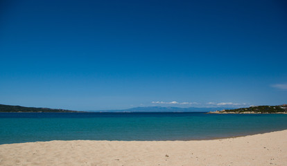 Fototapeta na wymiar Splendida spiaggia tranquilla con mare cristallino turchese e cielo blu a Porto Pollo, Sardegna. Sullo sfondo si vede la Corsica