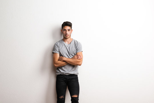 Cheerful young hispanic man standing in a studio, hands arms crossed. Copy space.