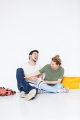 Fototapeta na wymiar Happy European young man and woman students sitting on floor isolated white wall background. Romantic cute couple enjoys spending studying time together and have fun. Education concept
