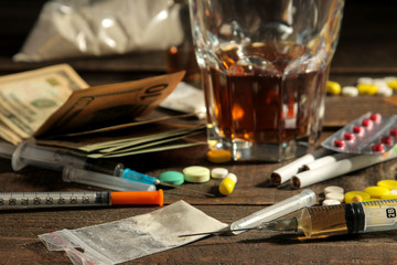 Various addictive drugs including alcohol, cigarettes, and drugs on a brown wooden table. Drug addiction concept