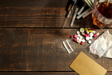 Various addictive drugs including alcohol, cigarettes, and drugs on a brown wooden table. top view with place for text.