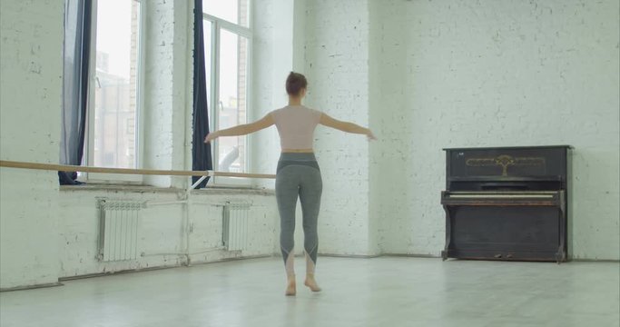Charming graceful ballerina rehearsing in ballet studio, performing soutenu exersice. Elegant classic ballet dancer practicing different choreograhic exercise and moves in dance studio.