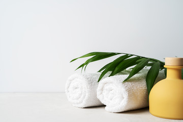 Spa concept: beautiful ceramic bottle, white towels and palm leaf on concrete light surface with...