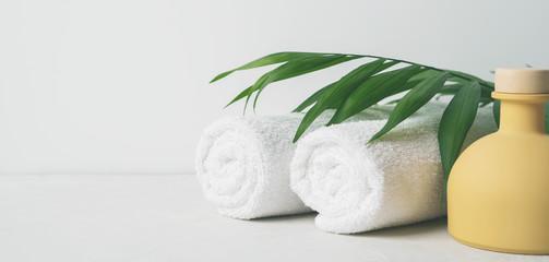 Spa concept: beautiful ceramic bottle, white towels and palm leaf on concrete light surface with copy space.