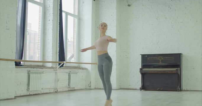 Charming graceful ballerina in sportswear rehearsing in ballet studio, performing soutenu exersice. Elegant classic ballet dancer practicing different choreograhic exercise and moves in dance studio.