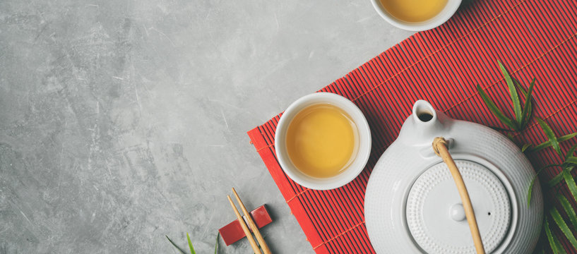 Asian food background with tea set and chopsticks on red bamboo mat on gray stone background. Top view with copy space.