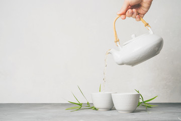 Female hand pouring green tea from a teapot into cups on white background with copy space. Asian...
