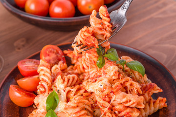 Portion of baked fusilli pasta with mozzarella cheese and tomato on a plate with a fork close-up, top view, rustic style
