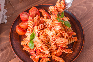 Portion of baked fusilli pasta with mozzarella cheese and tomato on a plate with a fork close-up, top view, rustic style