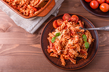 Portion of baked fusilli pasta with mozzarella cheese and tomato on a plate with a fork close-up, top view, rustic style
