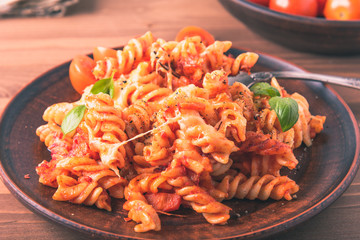 Portion of baked fusilli pasta with mozzarella cheese and tomato on a plate with a fork close-up, top view, rustic style