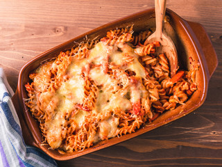 Fusilli pasta casserole with mozzarella cheese and tomato and wooden spoon, top view, close-up
