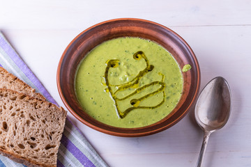 Pea cream soup in a clay plate and pieces of bread on a light background, top view